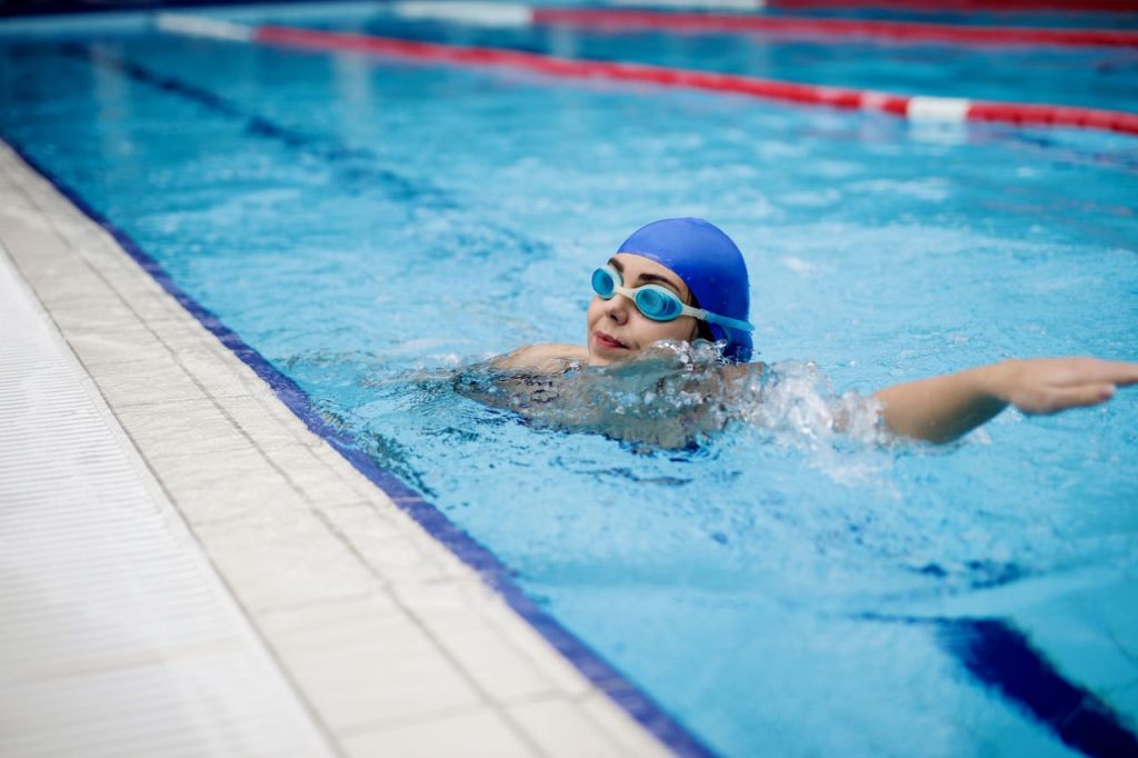Female swimmer in blue gear practicing strokes in an indoor swimming pool.